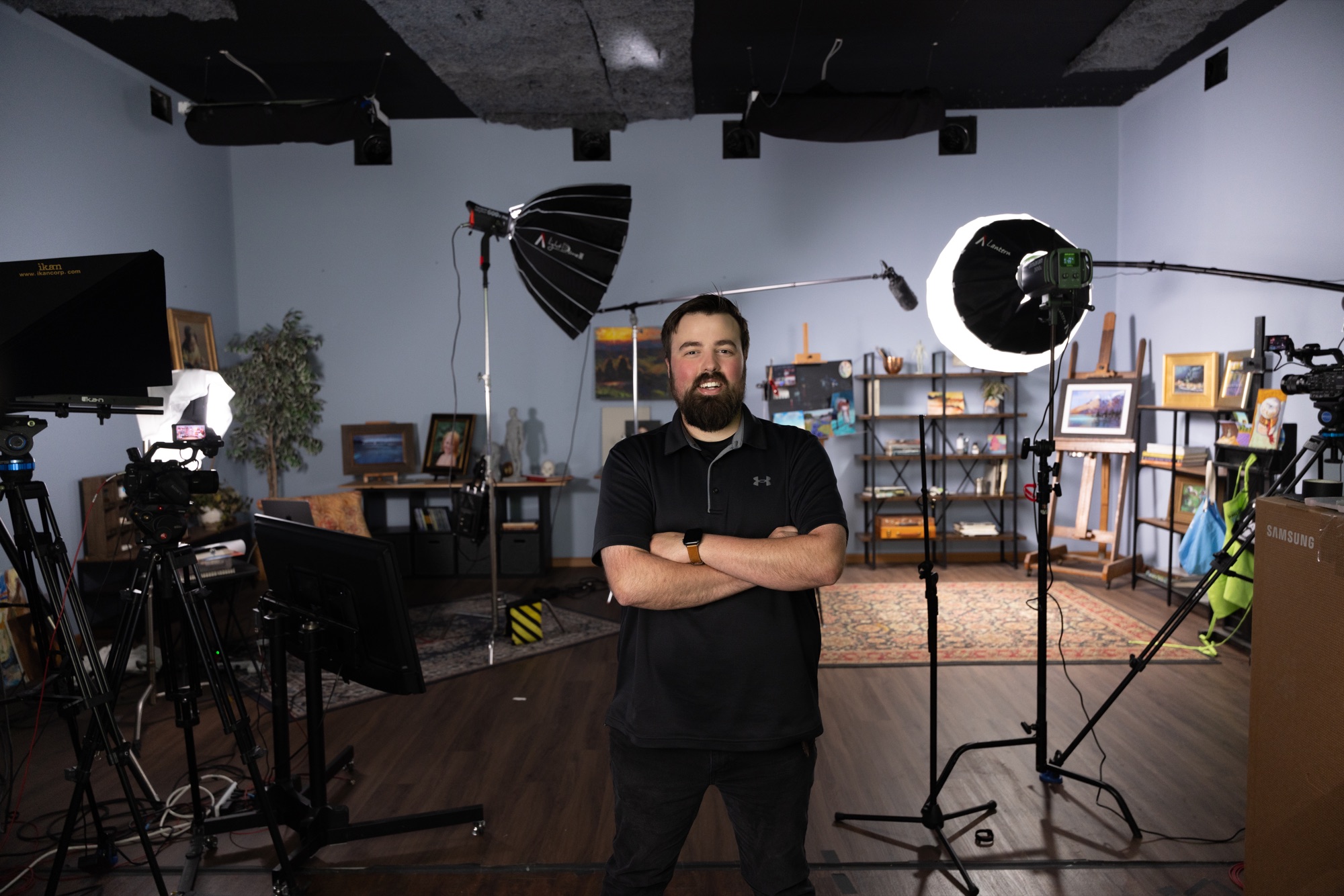 Arron Hartt standing on a working studio set surrounded by cameras, lighting, monitors, and audio equipment